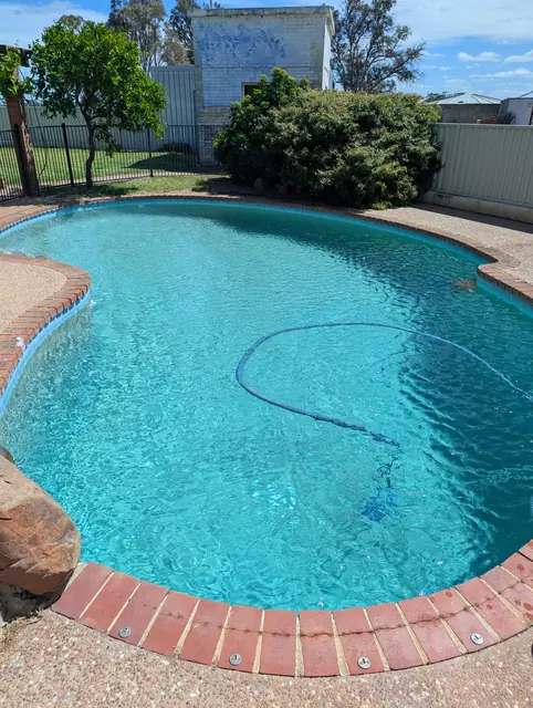 Clear turquoise kidney shaped pool with red brick coping