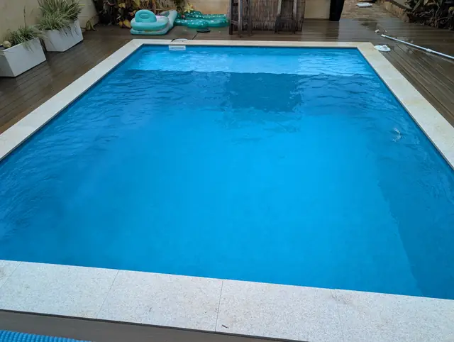 Bright blue pool with granite coping and a timber deck
