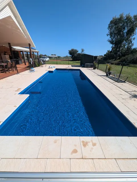 Long blue pool with sandstone pavers on a rural block