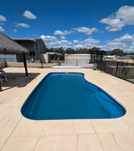 Curved blue pool with sandstone paving and a thatched umbrella