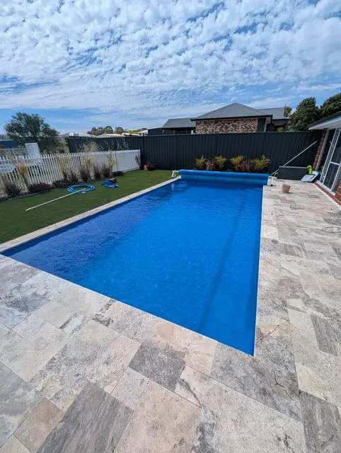 Blue pool with travertine paving, lawn and a solar cover roller
