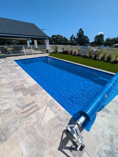 Bright blue pool with travertine paving and a solar cover roller